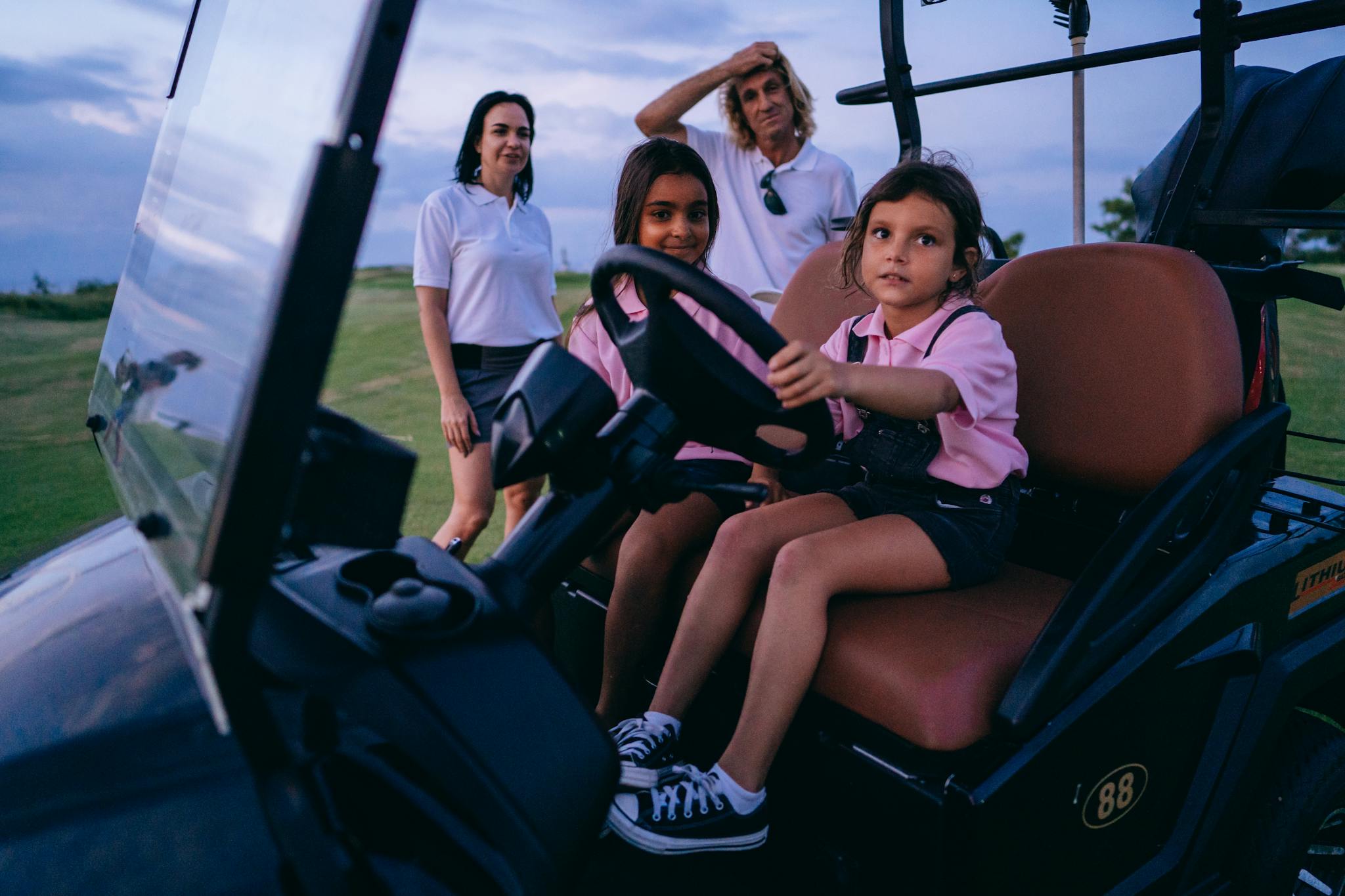 Family with kids having fun on a golf cart at a golf course during daylight.
