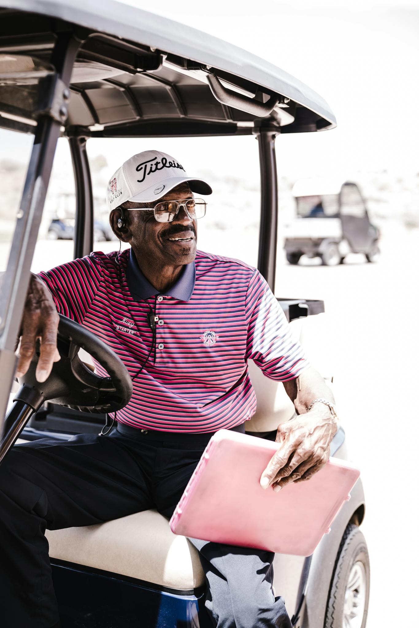 Smiling African American man with clipboard in a golf cart outdoors.